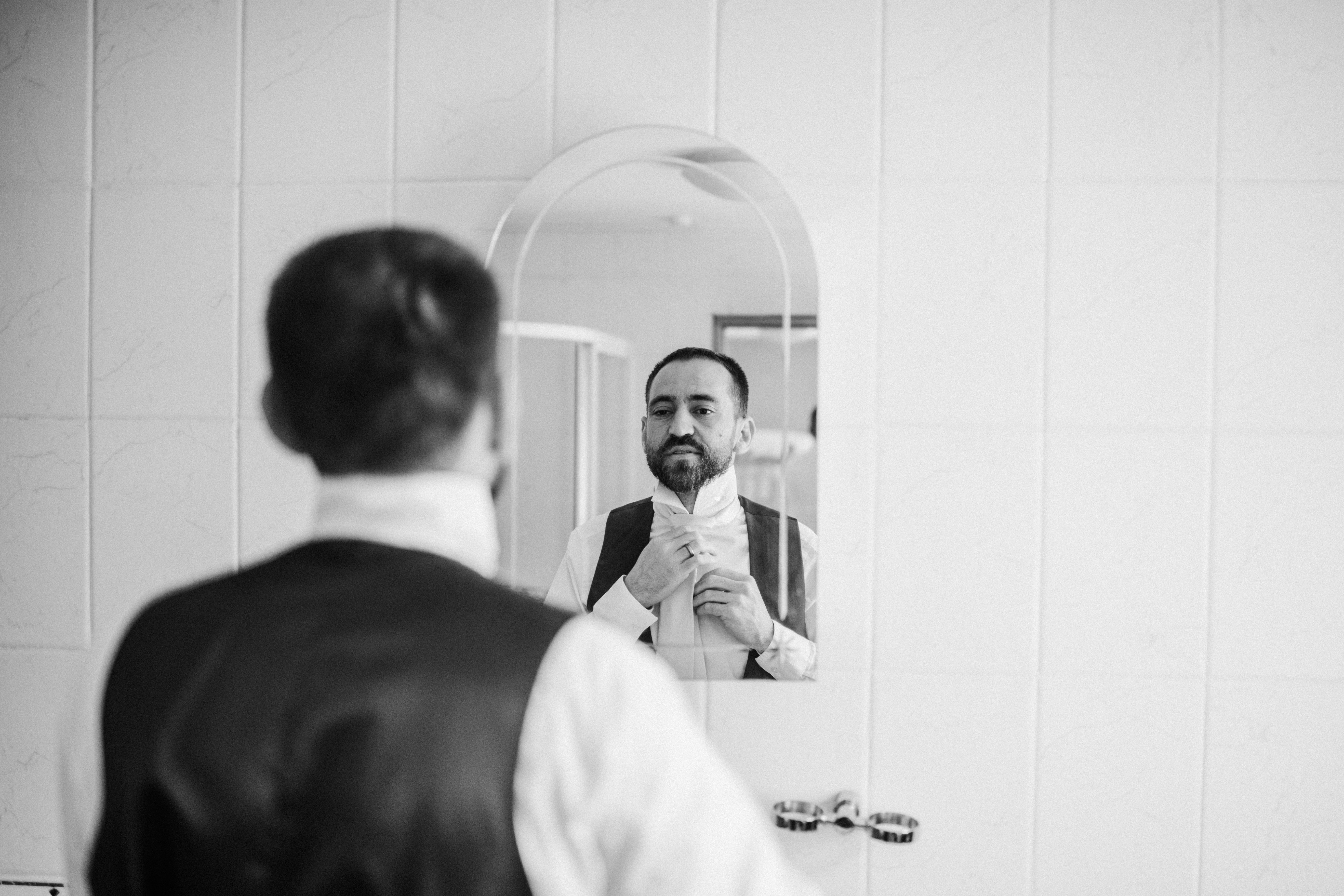 groom fixing tie at front of mirror